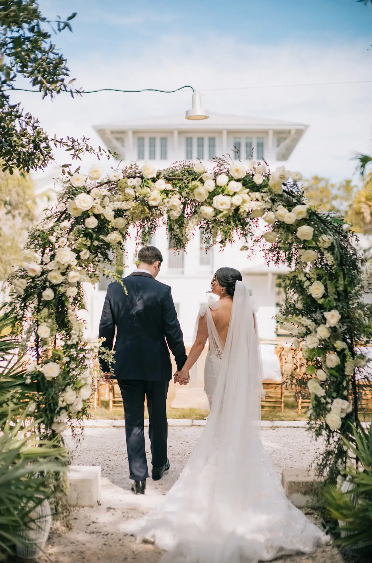 A bride and groom entering from the gate of white flowers.
